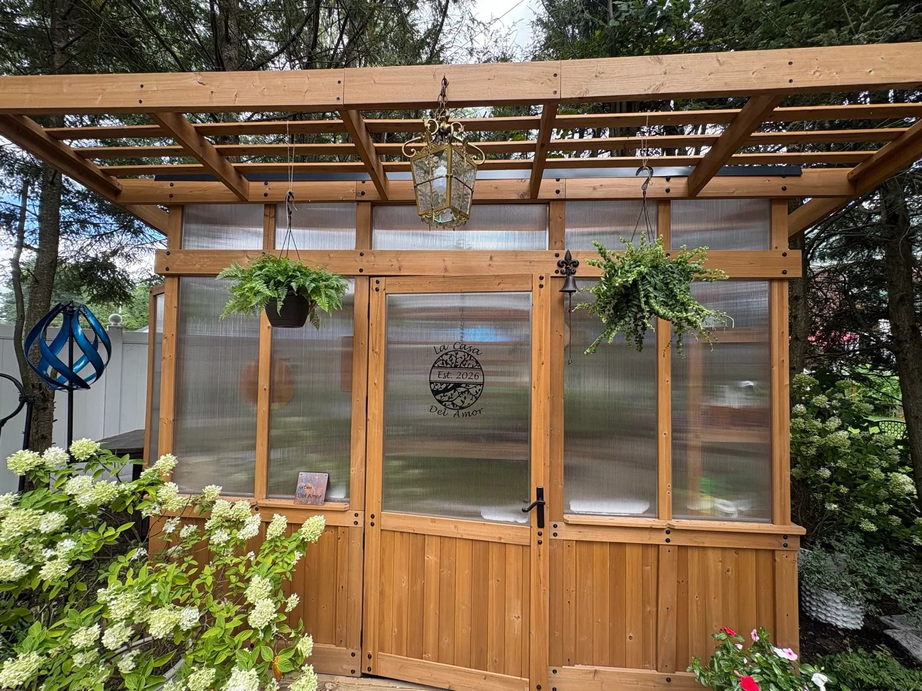 The cedar greenhouse behind Heather's house, hanging ferns at the door